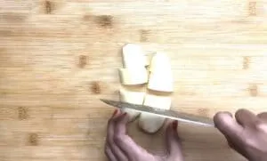 Person slicing potatoes on a wooden cutting board with a sharp knife.